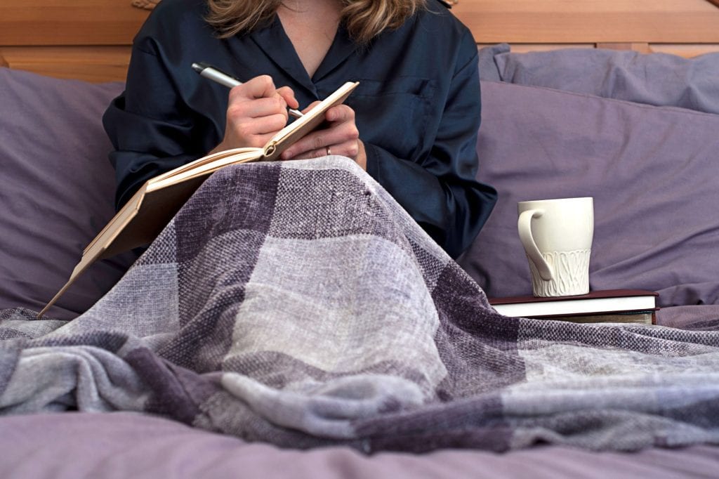 Woman writing in manifestation journal under blanket