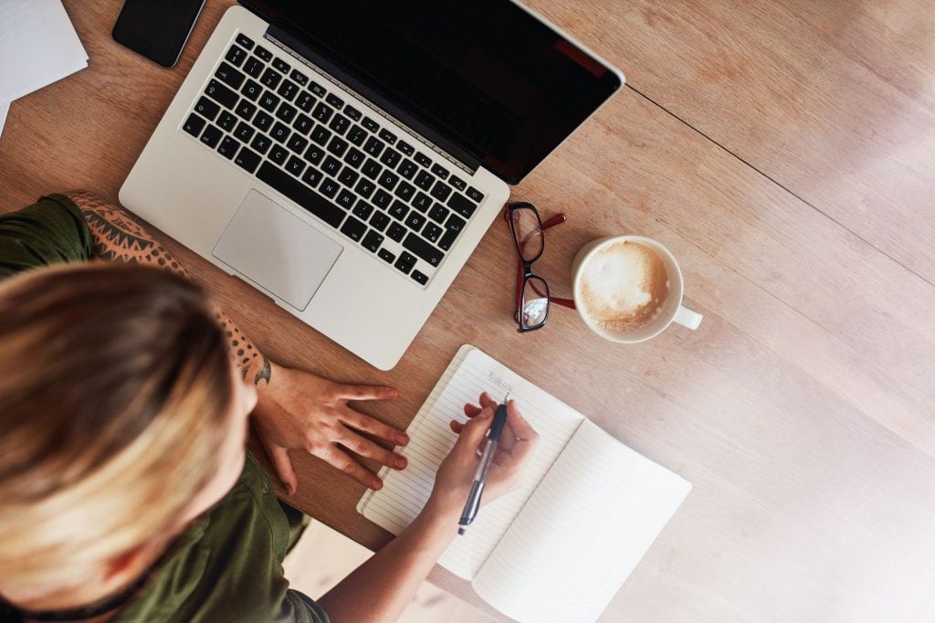Woman writing in a journal next to laptop