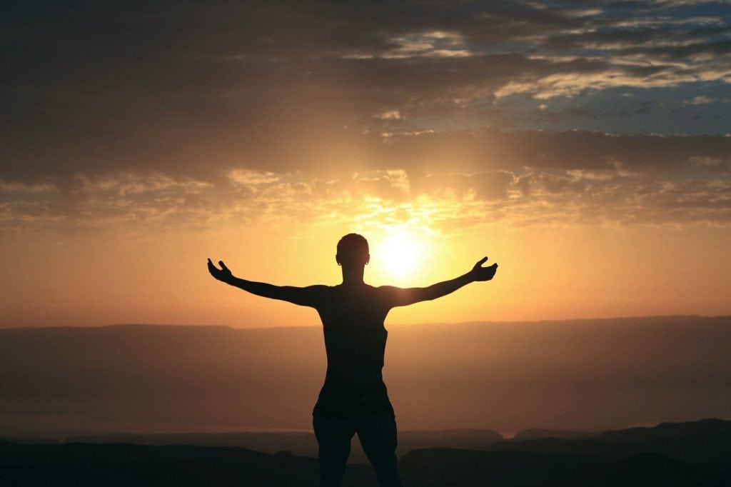 person with outstretched arms in front of sunset