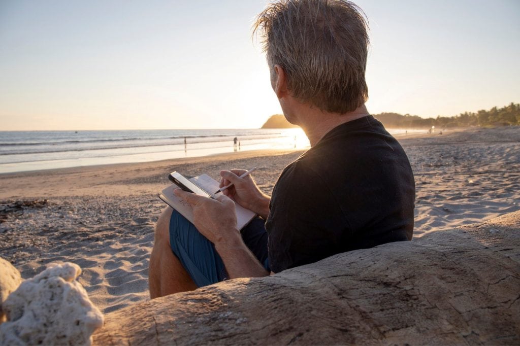 man writing in journal on beach