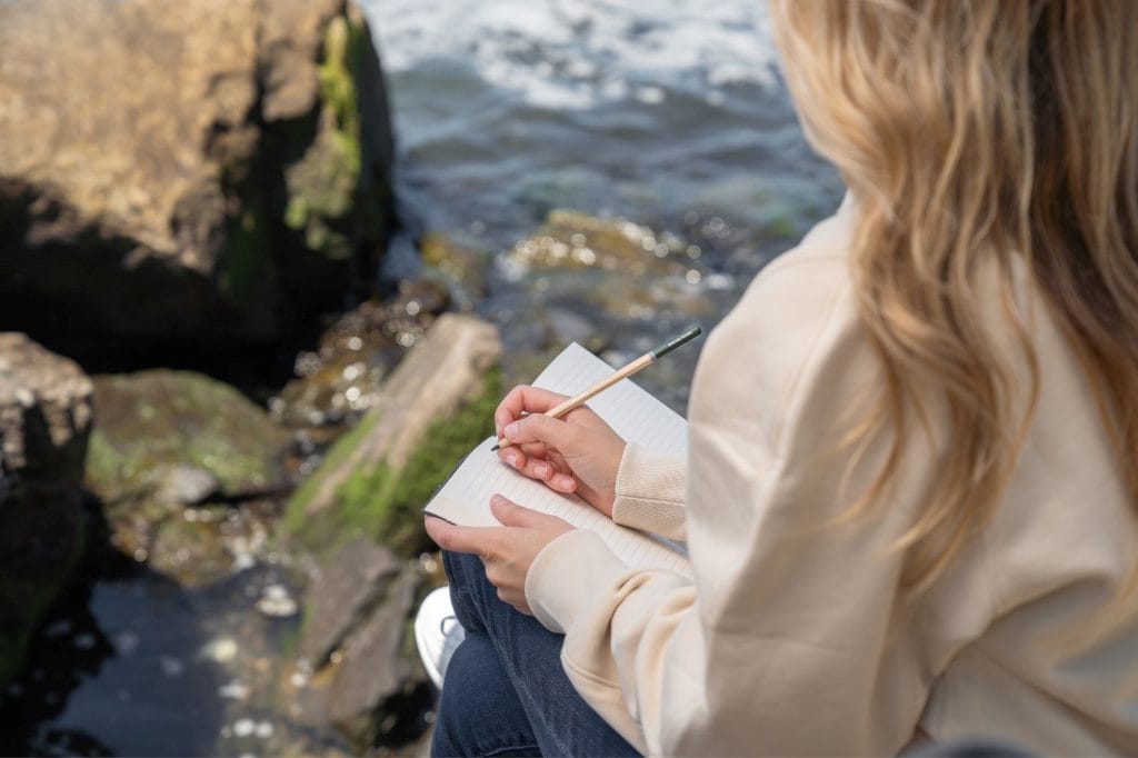woman writing in journal by water